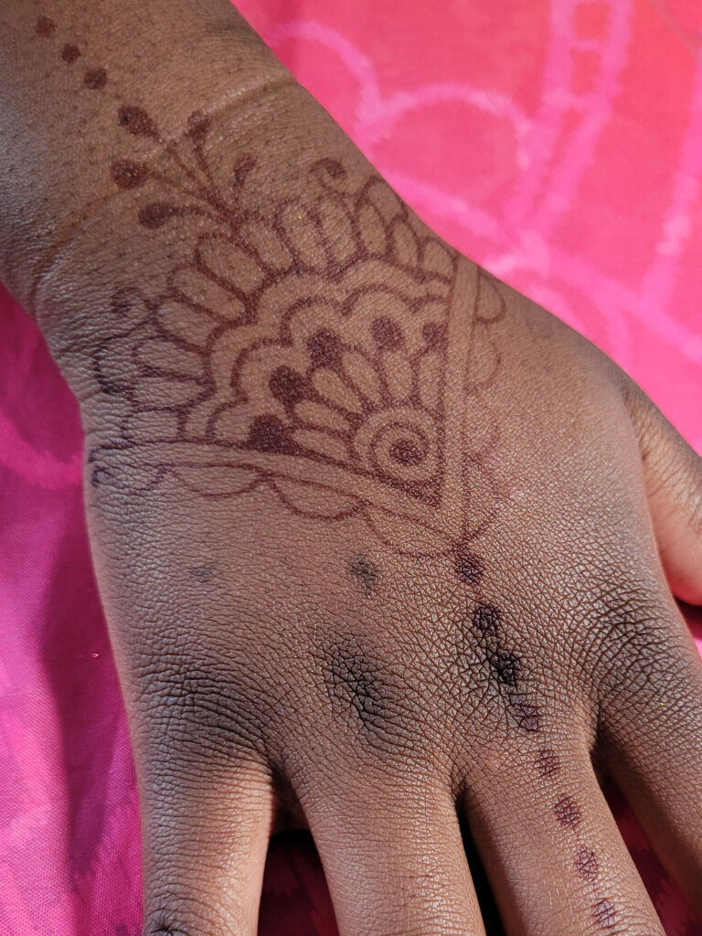 This is a picture of a burgundy henna stain on brown skin. The hand is on a pink background.