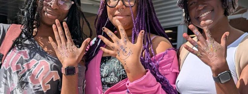 Three college students showing off there henna designs on dark skin.