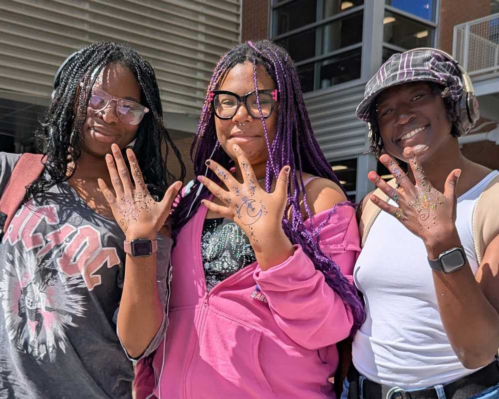 Three college students showing off there henna designs on dark skin.