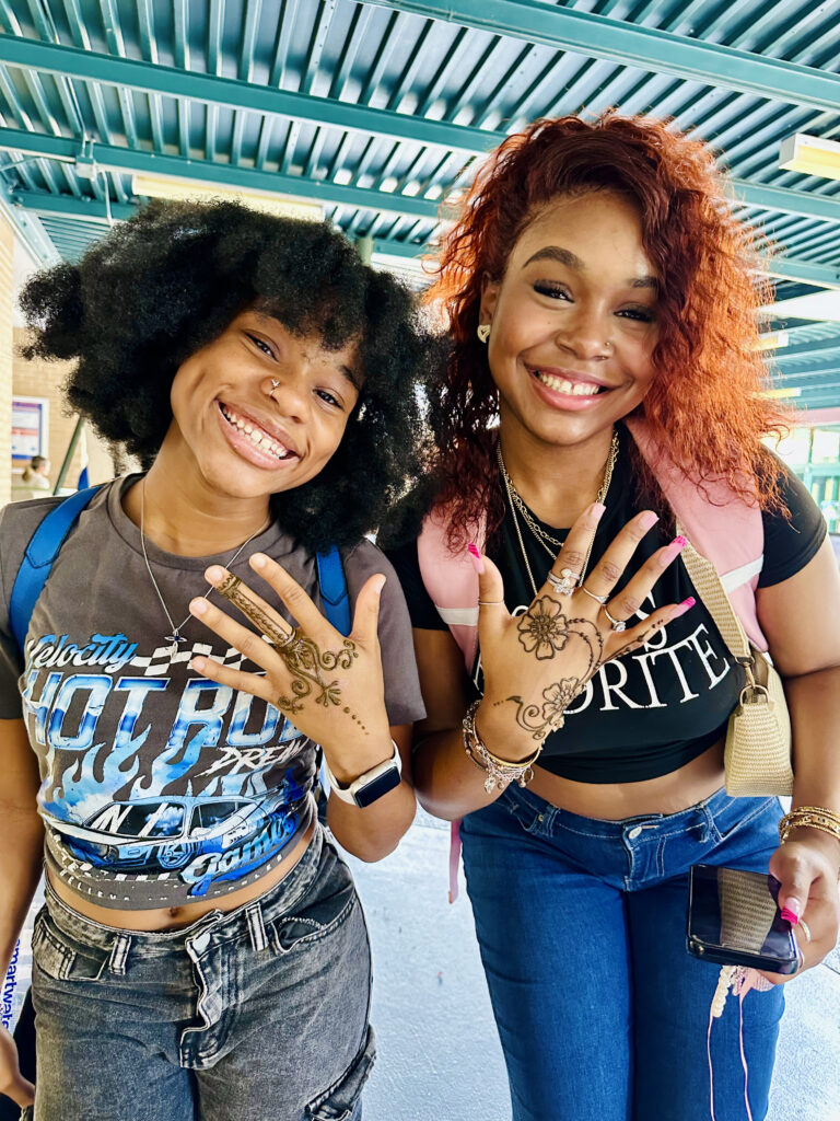Two pretty young women showing off henna designs on campus.